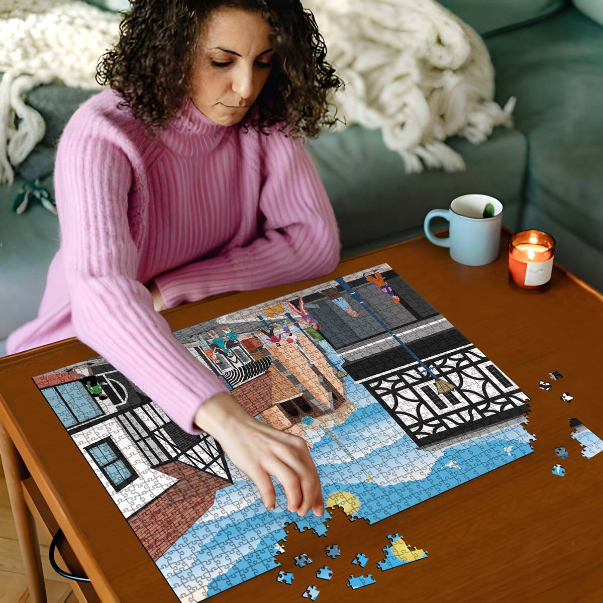 Woman in pink sweater working on a Hitchin town centre jigsaw puzzle on a wooden table with a cup and candles in the background