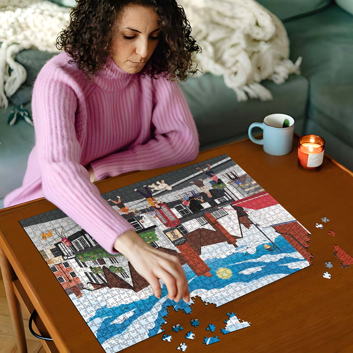 Woman in pink sweater working on a St Albans town centre jigsaw puzzle on a wooden table with a cup and candles in the background
