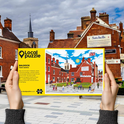 Hands holding "local Puzzle" box for Baldock Town Centre jigsaw puzzle in front of the actual location 