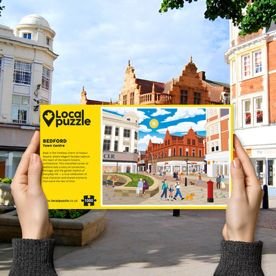 Person holding "local Puzzle" box for Bedford Town Centre jigsaw puzzle in front of the actual location 
