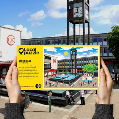 Person holding "local Puzzle" box for Stevenage Town Centre jigsaw puzzle in front of the actual location 