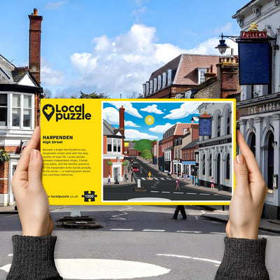 Hands holding "local Puzzle" box for Harpenden High Street jigsaw puzzle in front of the actual location 
