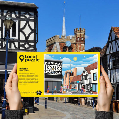 Person holding "local Puzzle" box for Hitchin Town Centre jigsaw puzzle in front of the actual location 