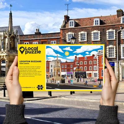 Hands holding "local Puzzle" box for Leighton Buzzard Town Centre jigsaw puzzle in front of the actual location 