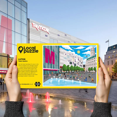 Person holding "local Puzzle" box for Luton Town Centre jigsaw puzzle in front of the actual location 