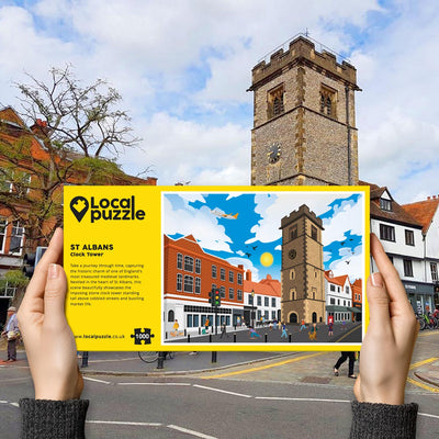 Person holding "local Puzzle" box for St Albans Clock Tower jigsaw puzzle in front of the actual location 