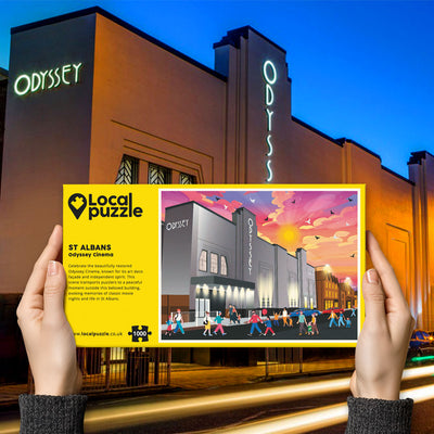 Person holding "local Puzzle" box for St Albans Odyssey Cinema jigsaw puzzle in front of the actual location 