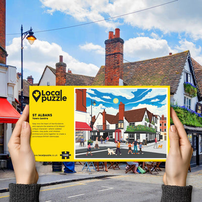 Person holding "local Puzzle" box for St Albans Town Centre jigsaw puzzle in front of the actual location 