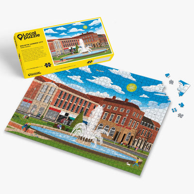 Welwyn Garden City Town Centre Jigsaw puzzle with a colourful scene of a town centre and yellow box packaging on a white background
