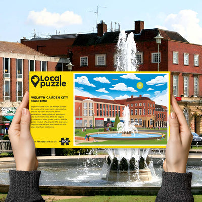 Hands holding "local Puzzle" box for Welwyn Garden City Town Centre jigsaw puzzle in front of the actual location 