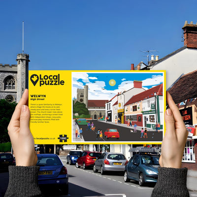 Hands holding "local Puzzle" box for Welwyn High Street jigsaw puzzle in front of the actual location 