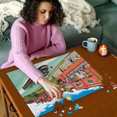 Woman in pink sweater working on Berkhamsted Grand Union Canal jigsaw puzzle on a wooden table with a cup and candles in the background