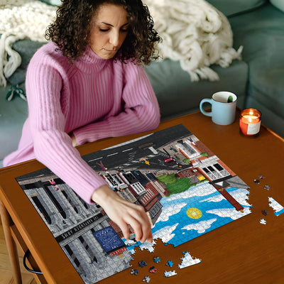 Woman in pink sweater working on a Harpenden High Street jigsaw puzzle on a wooden table with a cup and candles in the background