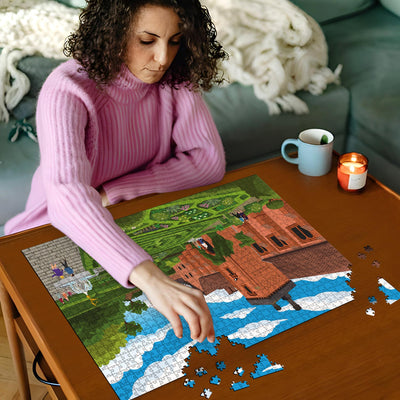 Woman in pink sweater working on a Hatfield Old Palace jigsaw puzzle on a wooden table with a cup and candles in the background