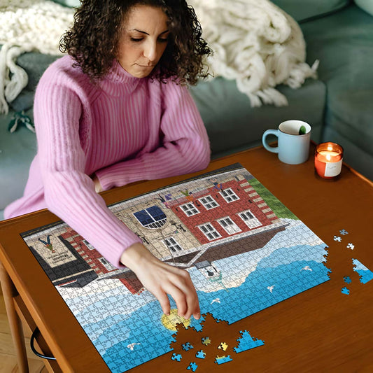 Woman in pink sweater working on a Hitchin town hall jigsaw puzzle on a wooden table with a cup and candles in the background