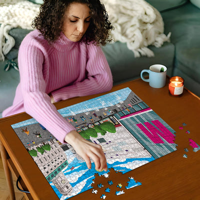 Woman in pink sweater working on a Luton town centre jigsaw puzzle on a wooden table with a cup and candles in the background
