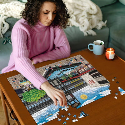 Woman in pink jumper working on a Stevenage town centre jigsaw puzzle on a wooden table with a cup and candles in the background