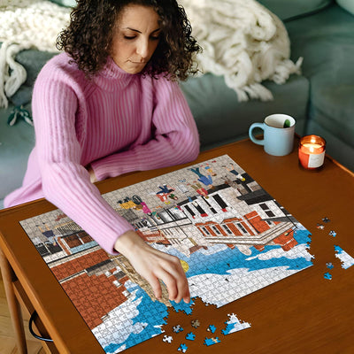 Woman in pink sweater working on a Waltham Cross town centre jigsaw puzzle on a wooden table with a cup and candles in the background