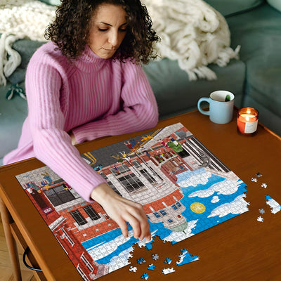 Woman in pink sweater working on a Watford town centre jigsaw puzzle on a wooden table with a cup and candles in the background