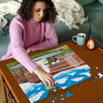 Woman in pink sweater working on a Welwyn Garden City Town Centre jigsaw puzzle on a wooden table with a cup and candles in the background