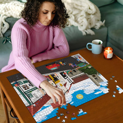 Woman in pink sweater working on a Welwyn High Street jigsaw puzzle on a wooden table with a cup and candles in the background